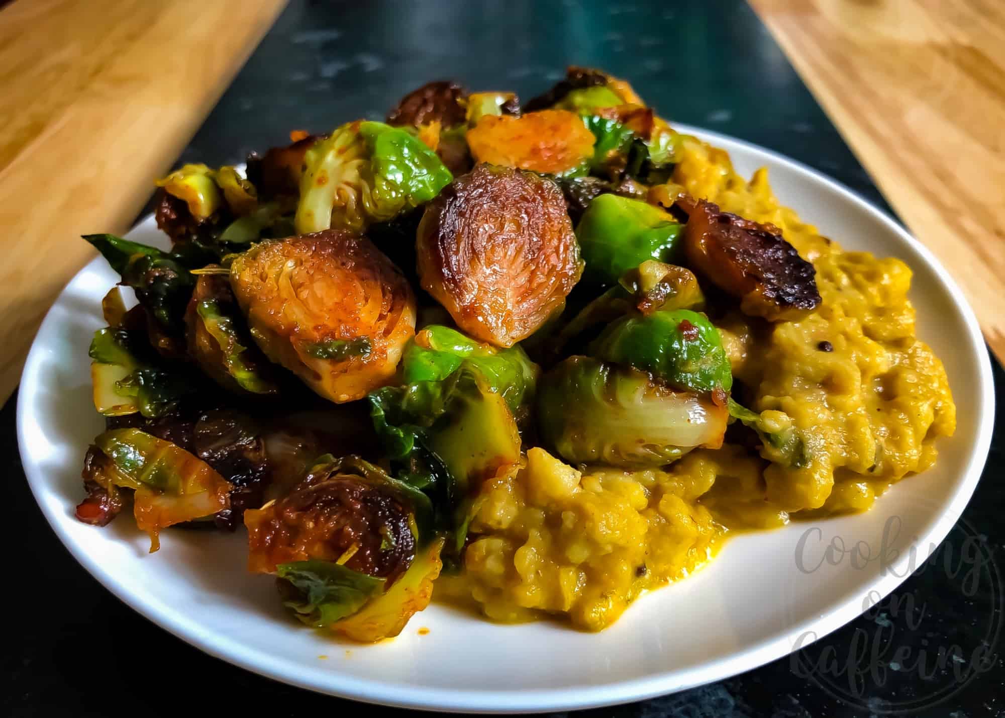 Side shot of seared Brussels sprouts coated in red chili paste and served on top of yellow dahl curry.